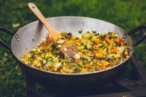 Colorful vegetable stir-fry cooking outdoors in a cast iron skillet for survival and camping meals.