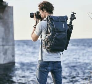 High-quality outdoor photographer with a professional camera, backpack, and safety gear by the water.