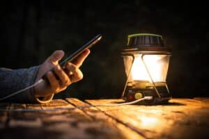 Bright outdoor camping lantern illuminating a dark evening scene with a smartphone in hand.