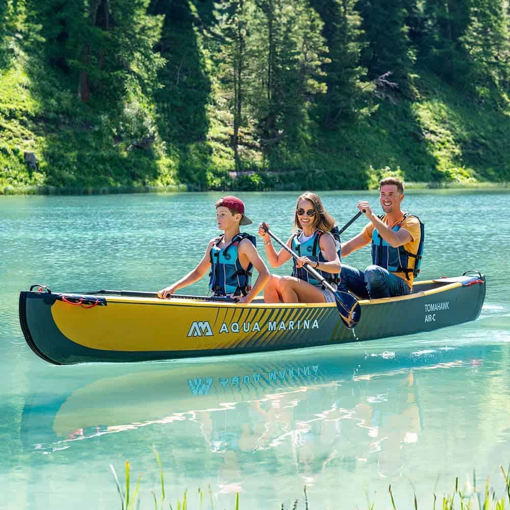 Bright outdoor adventure with friends kayaking on a clear lake in a waterproof kayak, surrounded by lush green forest.